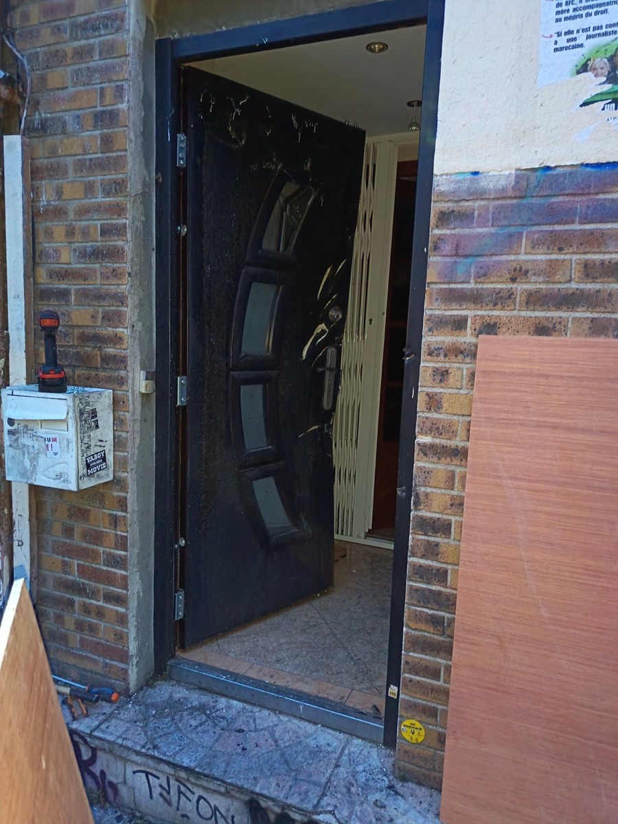 Entrée d'immeuble endommagée avec grille extensible de sécurité derrière la porte